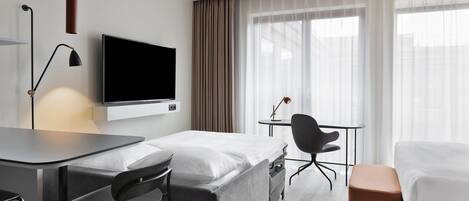 A hotel room with a bed, a desk, a chair, a TV, and a window with curtains.