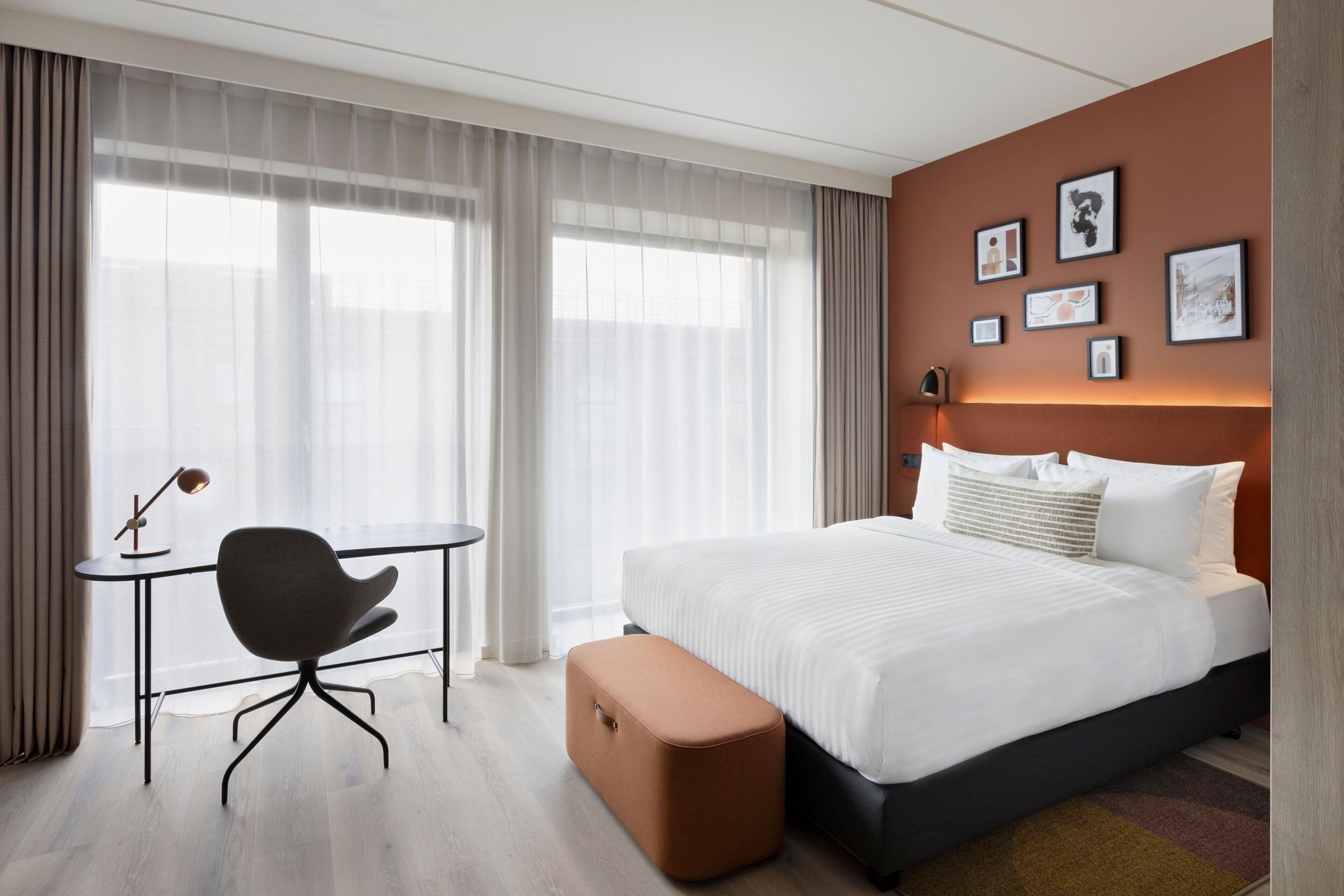 A modern hotel room with a bed, a desk, and a chair.