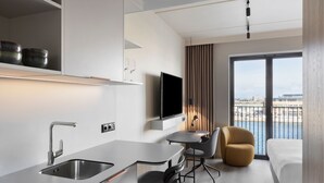 Une chambre d’hôtel moderne dotée d’un coin cuisine, d’une table à manger avec des chaises, d’un canapé et d’une grande fenêtre offrant une vue sur la ville.