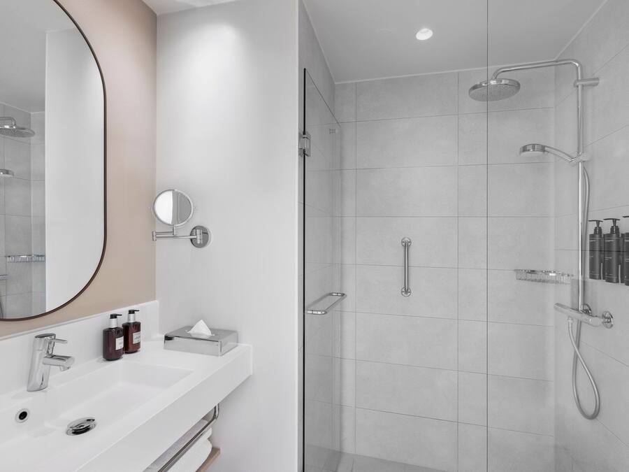 Un baño moderno con un espejo grande, un lavabo blanco y una zona de ducha con mampara de cristal.