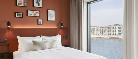 Una habitación de hotel con una cama grande, vistas a la ciudad y obras de arte en la pared.