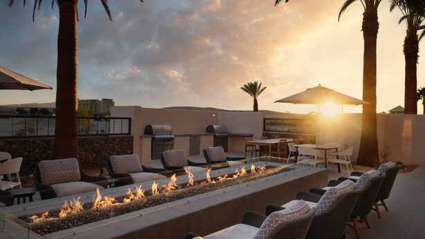 Un patio al aire libre con un amplio hogar de fuego, asientos y sombrillas.