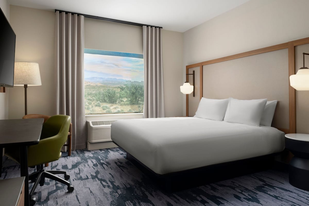 A hotel room with a large bed, a desk, a chair, a TV, and a view of the outdoors.