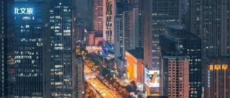 A cityscape at dusk with illuminated buildings and a busy highway.