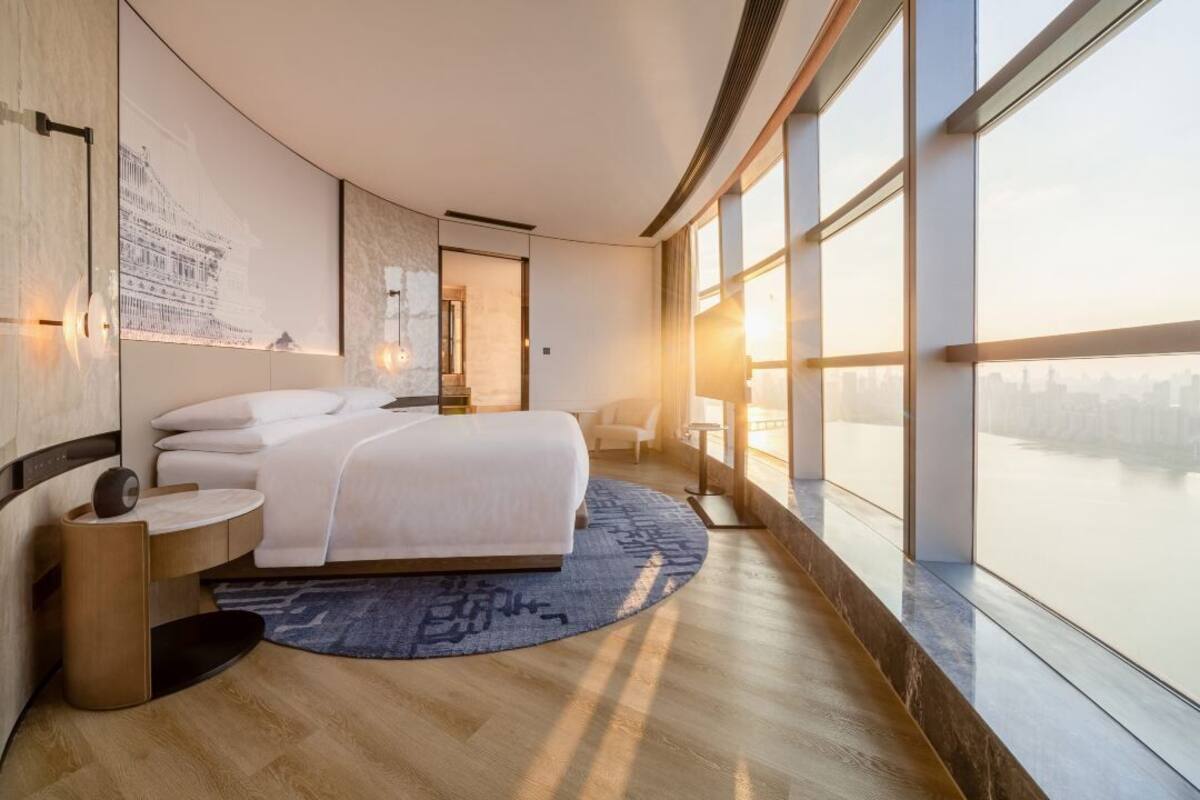 A modern hotel room with a large bed, a view of the city, and a large window.