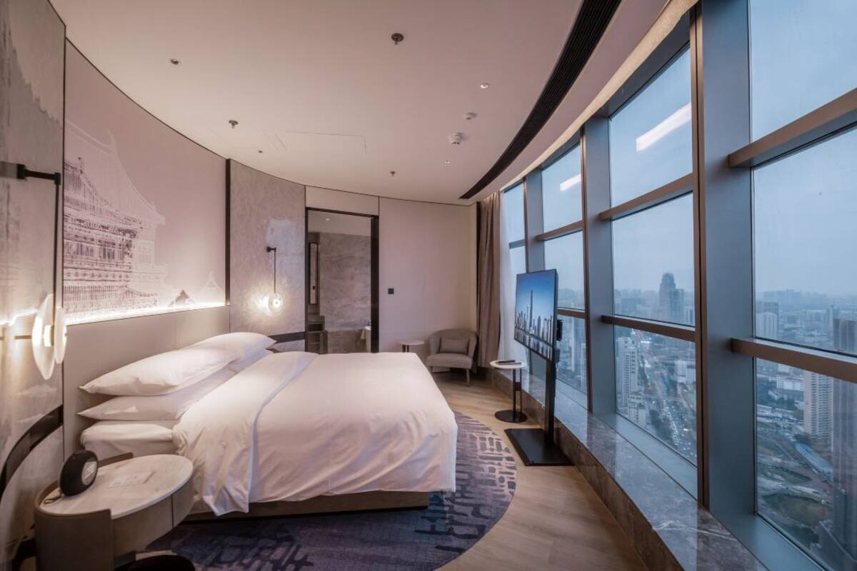 A modern hotel room with a large bed, a TV, and a city view.