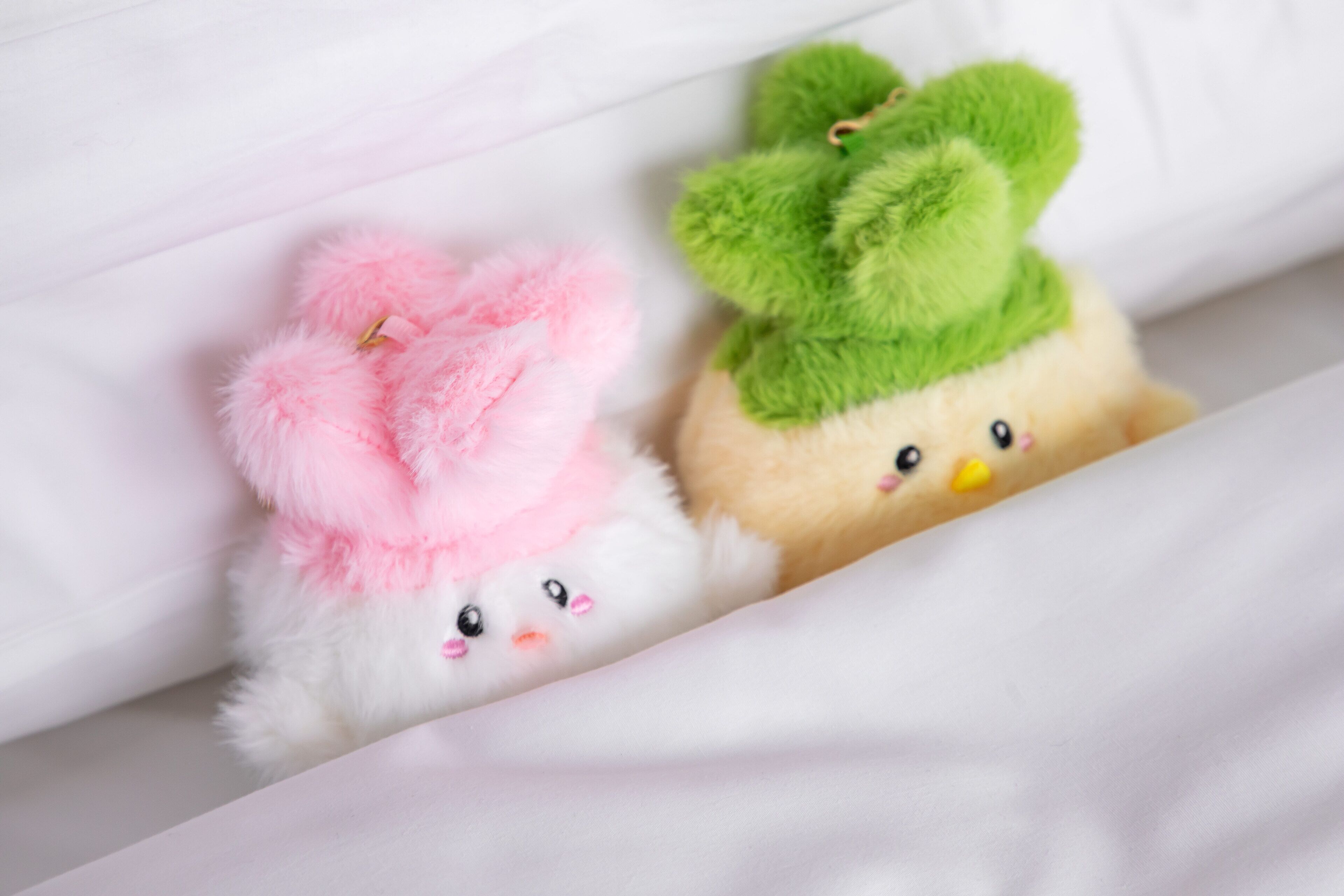 Two plush toys, one pink and one green, on a white bed.