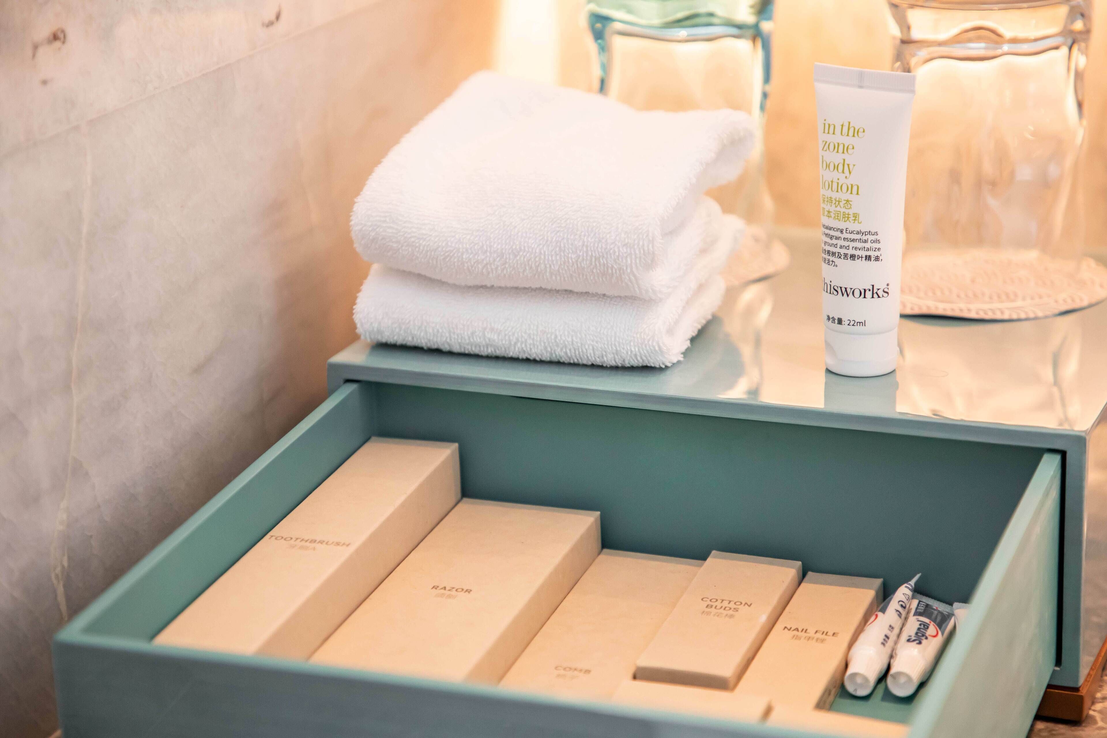 A bathroom vanity with neatly arranged toiletries including a tube of body lotion, a folded white towel, and several toiletry boxes.