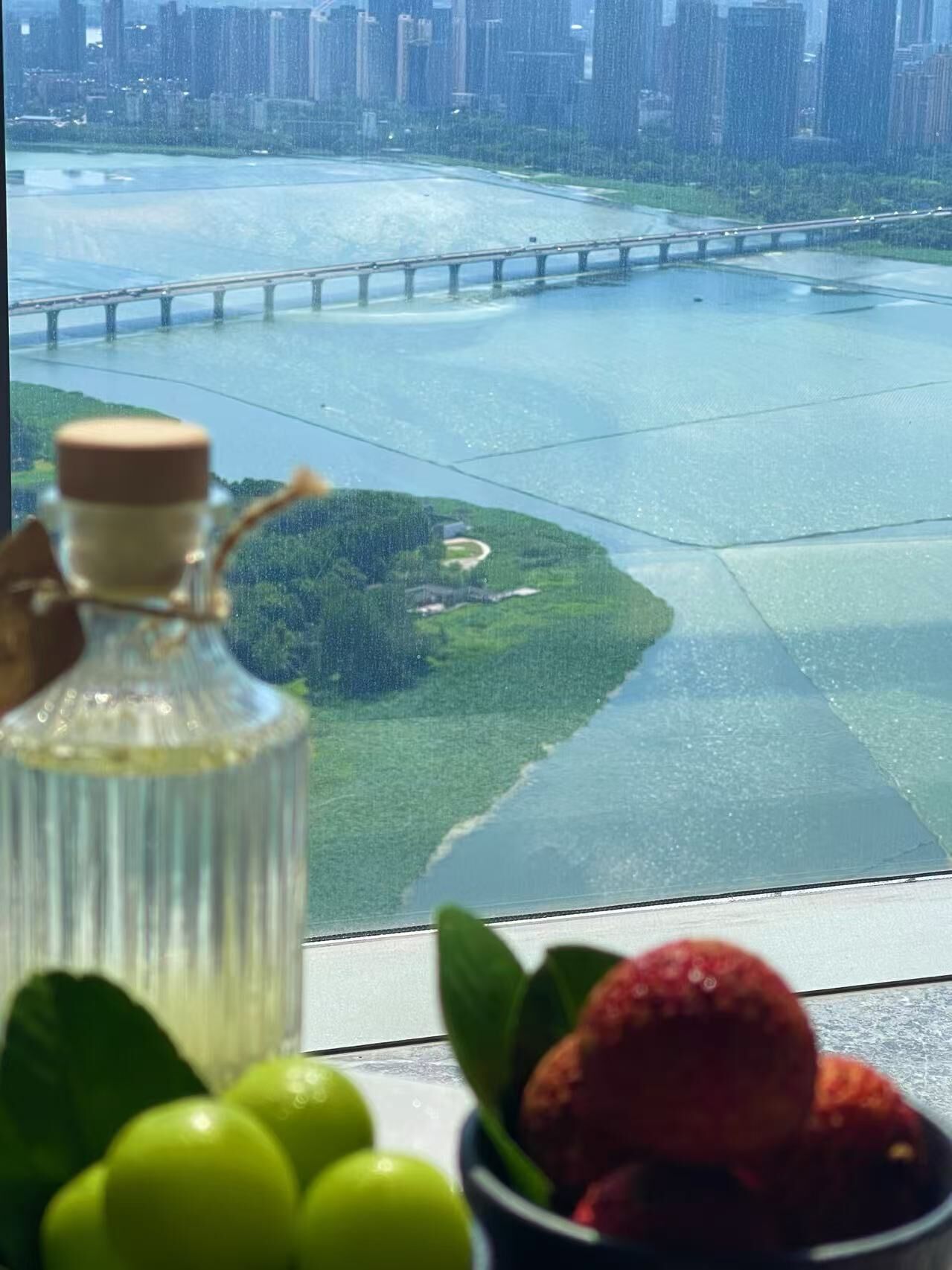 A view from a window overlooking a river with a bridge, a green area, and a bottle of oil in the foreground.