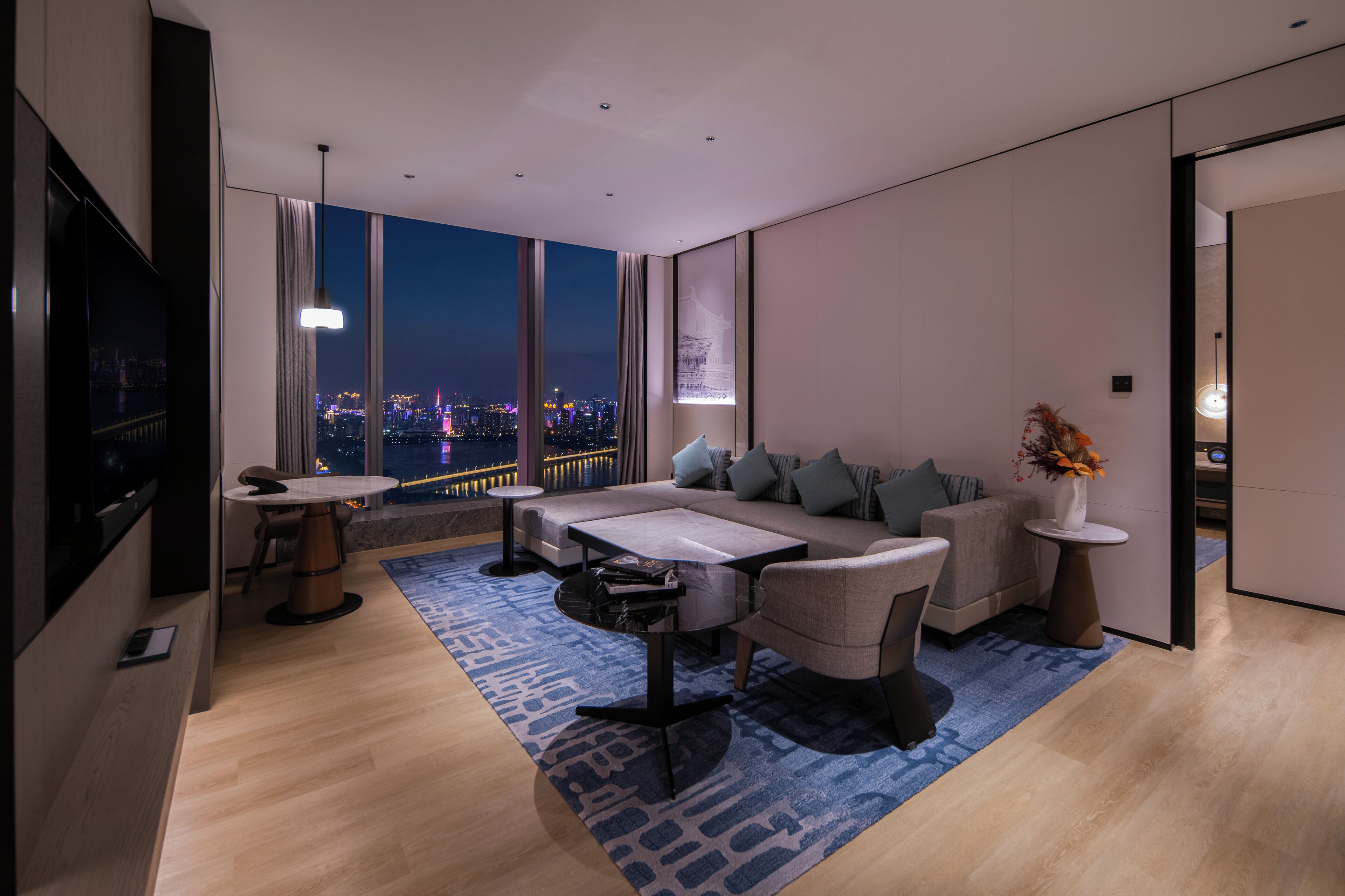 A modern living room with a large window offering a city view, a sofa, a coffee table, and a TV.
