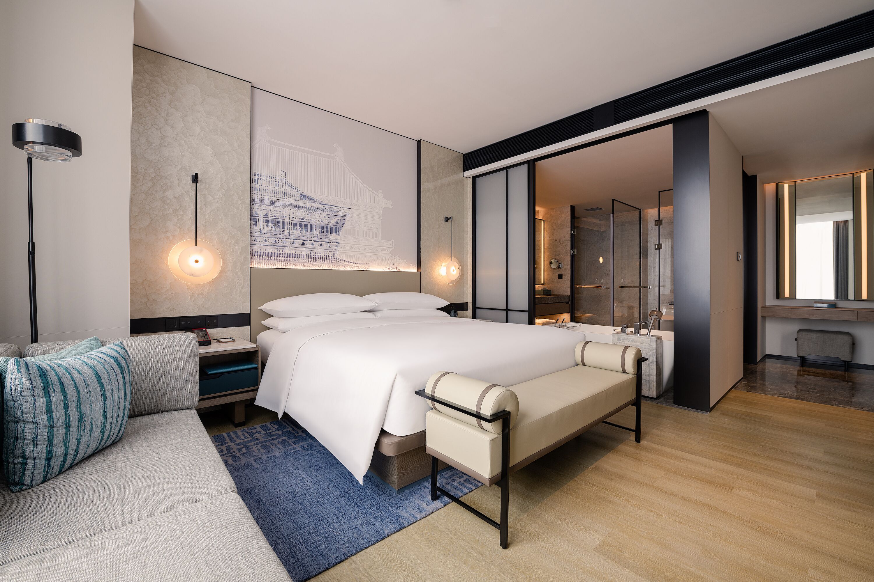 A modern hotel room with a large bed, a seating area, a bathroom, and a view of a traditional building.
