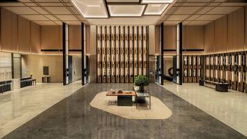 A spacious lobby with a central seating area, a reception desk, and a decorative wall with vertical elements.