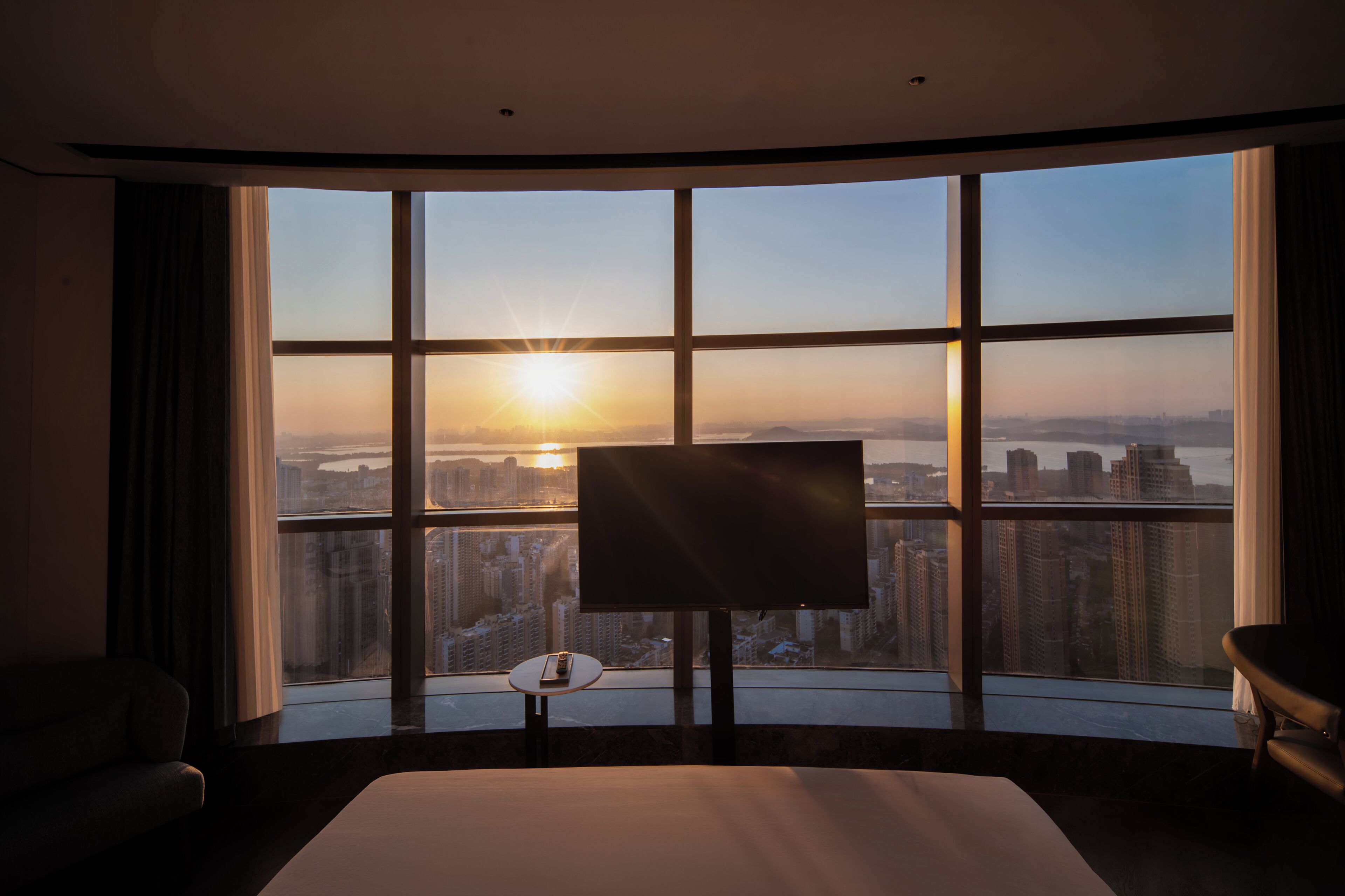 Una camera d'albergo con un'ampia finestra, un letto, una TV e un tavolino.