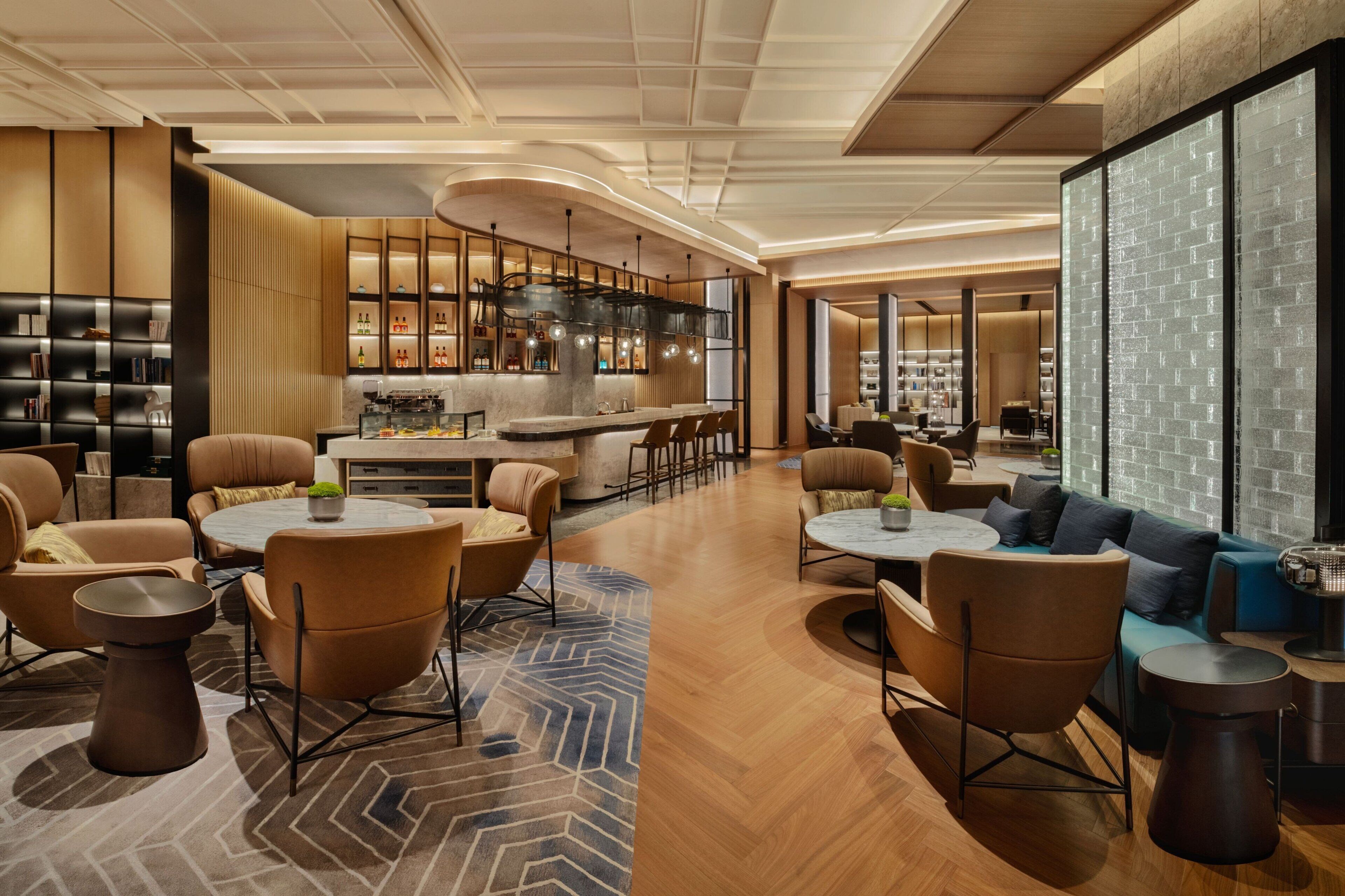 A modern hotel lobby with a central bar, seating areas, and a large brick wall.