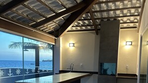 A modern kitchen with a central island, a built-in oven, and a view of the sea through large windows. - Village no Condominio Arauá, Fechado com Trilha Para Caminhada, Academia (Condomínio Arauá Vera Cruz)