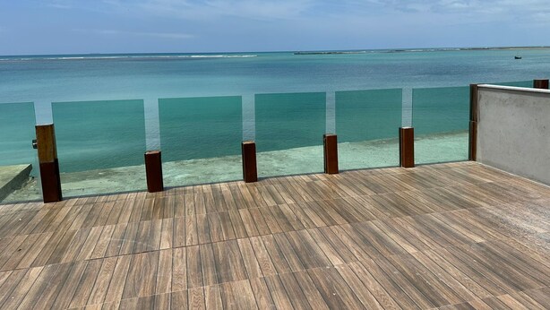 A wooden deck with a glass barrier overlooking a clear blue sea and a distant shoreline. - Village no Condominio Arauá, Fechado com Trilha Para Caminhada, Academia (Condomínio Arauá Vera Cruz)