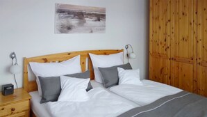 A double bed with white and gray bedding, two bedside tables with lamps, and a wooden wardrobe. - Maisonette apartment for 4 persons, washing machine, WLAN, parking lot, quiet location (Prerow)