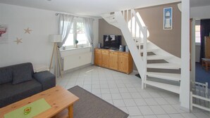 A living room with a sofa, a wooden table, a TV, a cabinet, and a staircase. - Maisonette apartment for 4 persons, washing machine, WLAN, parking lot, quiet location (Prerow)