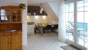 A dining area with a table and chairs, a kitchen with a stove and cabinets, and a large window with a view. - Maisonette apartment for 4 persons, washing machine, WLAN, parking lot, quiet location (Prerow)