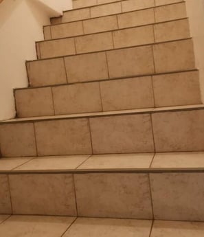 Eine Treppe mit beigen Fliesen und einem Geländer auf der rechten Seite.