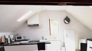 Une cuisine avec un coin repas, comprenant une table recouverte d’une nappe, des chaises et une horloge au mur.