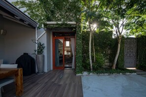 A wooden deck leading to a glass door, surrounded by greenery and a concrete area. - Franschhoek Homestead Cottage (Franschhoek)