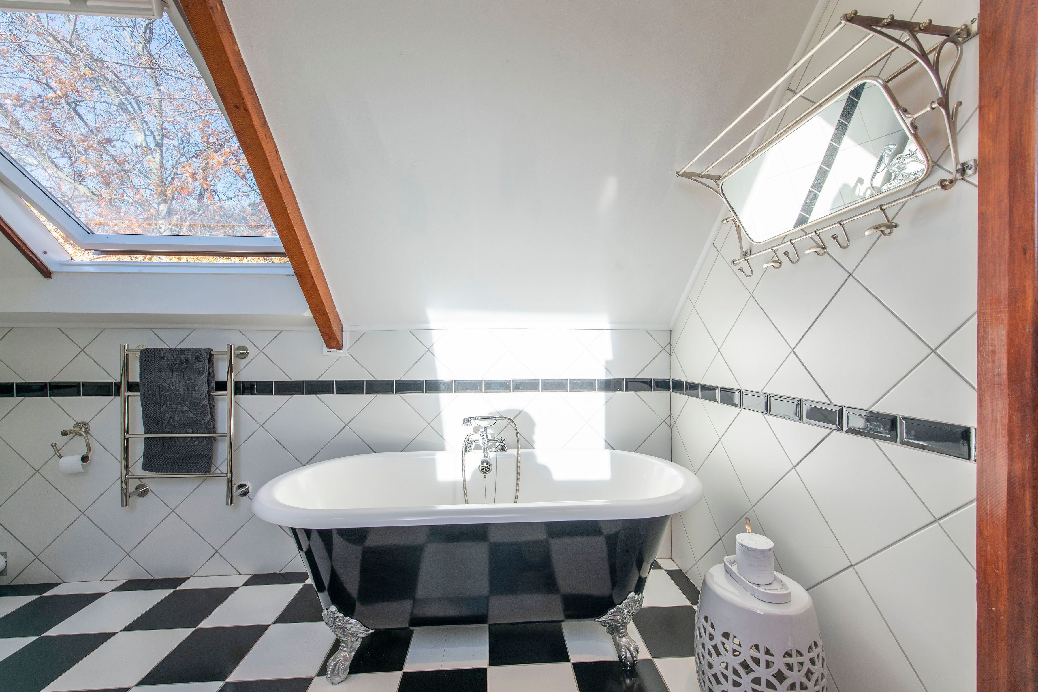 A bathroom with a freestanding bathtub, a skylight, and a mirror with a metal frame.