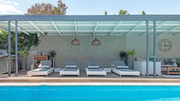 A covered outdoor seating area with lounge chairs and a pool. - Franschhoek Homestead Cottage (Franschhoek)