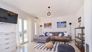 Un salon moderne avec un canapé, un pouf et une table basse, un téléviseur à écran plat fixé au mur et des œuvres d’art accrochées aux murs.
