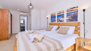 Une chambre d’hôtel moderne avec un grand lit, une tête de lit en bois et une œuvre d’art représentant un coucher de soleil sur un paysage rocheux.