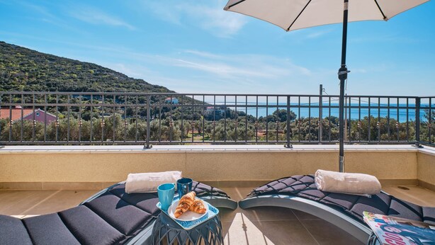 Un balcon avec deux fauteuils, une table avec un croissant et une tasse bleue, et un grand parasol.