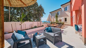 An outdoor patio with wicker furniture, a table with a blue cup, and a hanging chair. - MEACres Sun - secluded pool villa (Miholašćica)