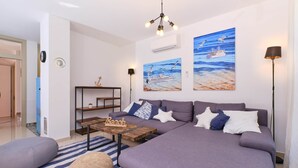 A modern living room with a large sofa, a coffee table, and a bookshelf. There are two paintings on the wall depicting seagulls and a ship. - MEACres Sun - secluded pool villa (Miholašćica)