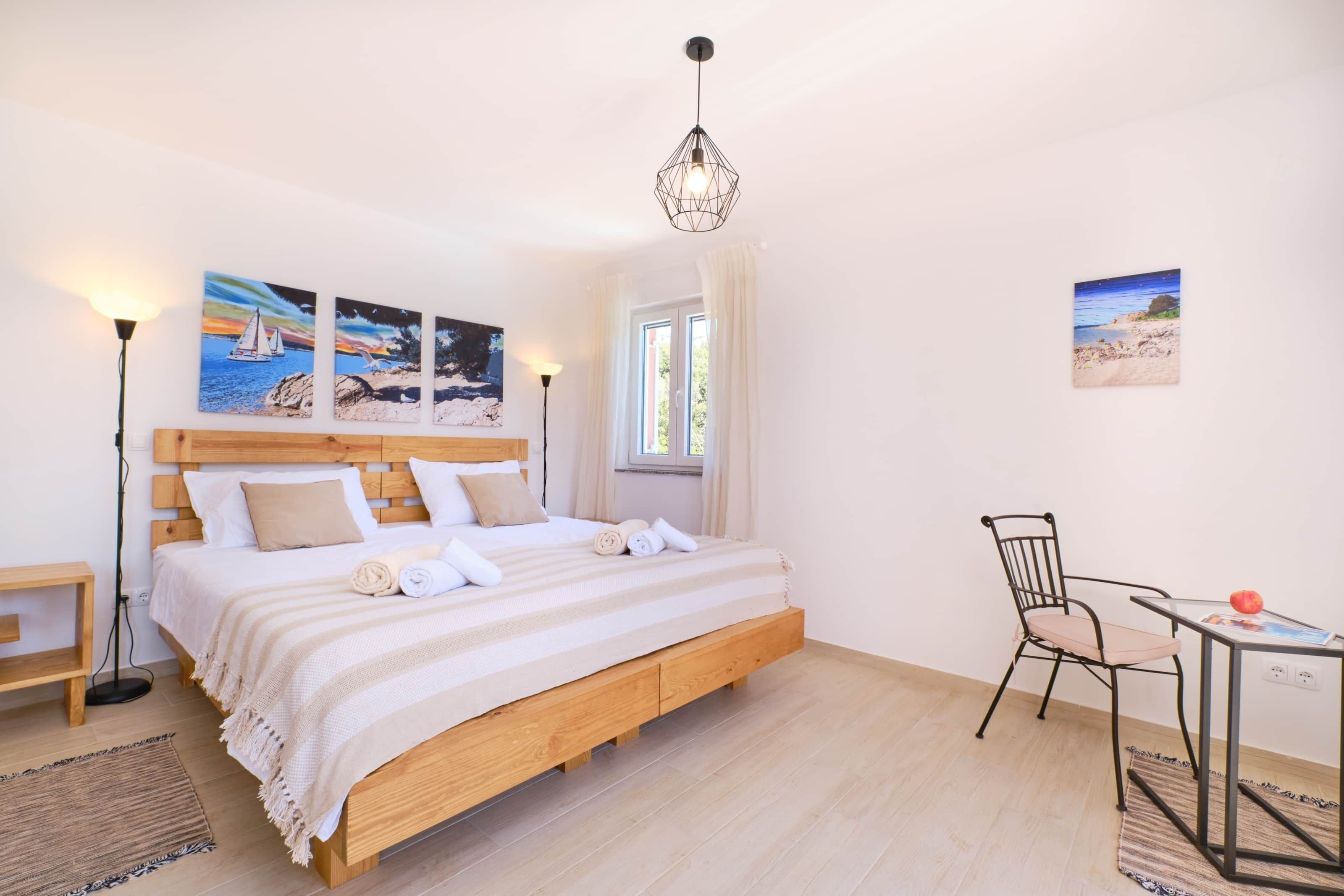 Un dormitorio con cama de madera, una silla, una mesa y obras de arte en las paredes.