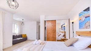 A modern bedroom with a large bed, a sofa, a wooden wardrobe, and a painting of a sailboat. - MEACres Sun - secluded pool villa (Miholašćica)