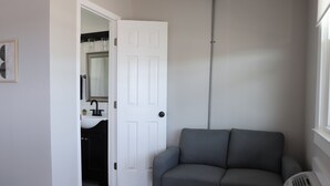 A room with a gray sofa, a white door, a bathroom with a sink and mirror, and a radiator. - Inviting 1BR 10-Mins to Nashville (Nashville)