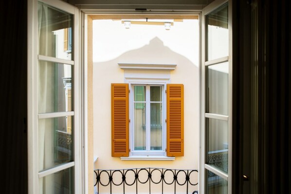 A building with a window and shutters, a balcony with a metal railing, and a mountain in the background.