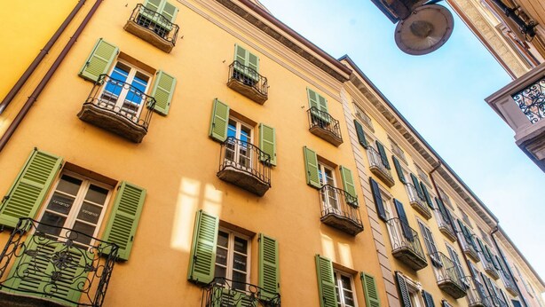 Um edifício com várias janelas, algumas com persianas verdes, e varandas com grades de metal.