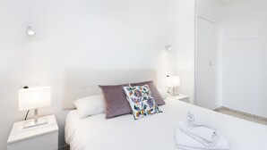 Ein Hotelzimmer mit einem ordentlich bezogenem Bett, zwei Nachttischen mit Lampen, einem weißen Kleiderschrank und einer Tür zu einem Badezimmer.
