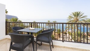 Ein Balkon mit Tisch und Stühlen, der Blick auf einen Strand mit Palmen und das Meer freigibt.