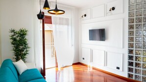 Una sala de estar con un sofá color turquesa, un televisor montado en la pared y piso de madera.