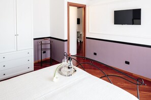 Een slaapkamer met een bed, een kaptafel, een aan de muur bevestigde televisie en een deur naar een andere kamer.