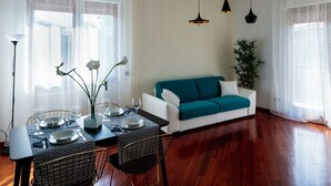 Un comedor con una mesa preparada para cuatro personas, un sofá y una planta en maceta.