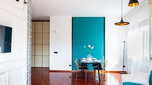 Una sala moderna con una pared de acento color turquesa, una zona de comedor con mesa y sillas de vidrio, y un sofá con cojín turquesa.