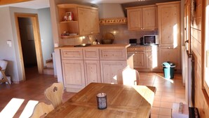 A kitchen with wooden cabinets, a microwave, and a dining table with chairs. - Large, very bright chalet for 8 people with large terrace, garden and a beautiful open view.Interior (St-Luc)