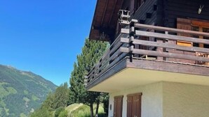 A wooden chalet with a balcony, surrounded by a grassy area and trees, overlooking a mountainous landscape. - Large, very bright chalet for 8 people with large terrace, garden and a beautiful open view.Interior (St-Luc)