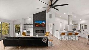 A modern living room with a fireplace, a dining area with bar stools, and a kitchen with white cabinets. - Spectacular Red Rock Views in West Sedona! (Sedona)