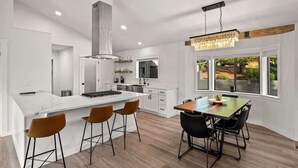 A modern kitchen with a large island, bar stools, a dining table with chairs, and a view of the outdoors through large windows. - Spectacular Red Rock Views in West Sedona! (Sedona)