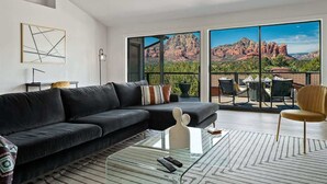 A modern living room with a black sofa, a glass coffee table, and a view of red rock formations through large windows. - Spectacular Red Rock Views in West Sedona! (Sedona)