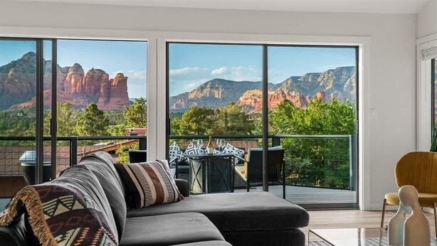 A modern living room with a sectional sofa, a dining table, and chairs. It features large windows with a mountain view. - Spectacular Red Rock Views in West Sedona! (Sedona)